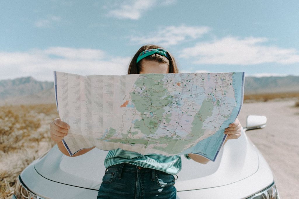 Woman leaning on the hood of a car, reading a map