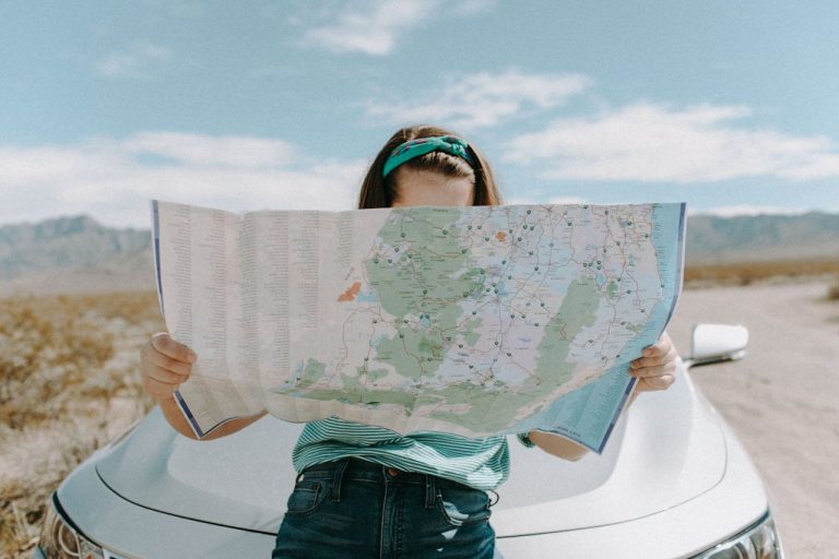 Woman leaning on the hood of a car, reading a map